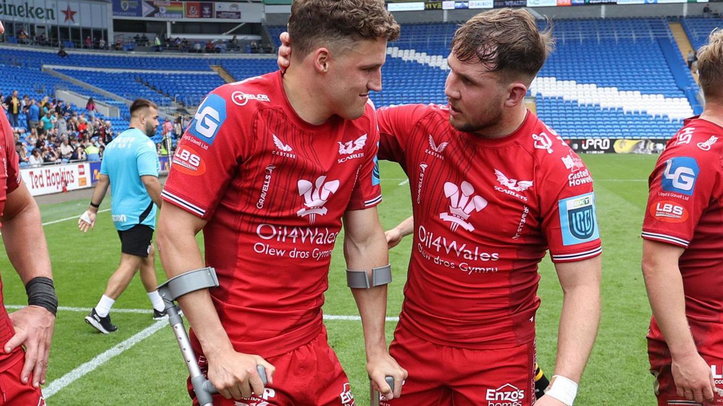 Tomi Lewis is consoled by Ioan Lloyd after being on crutches and having his foot in a protective boot after helping Scarlets beat Dragons