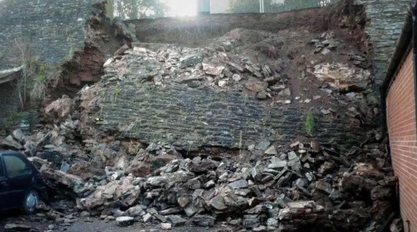 A collapsed grey stone wall with blocks of stone, including one large section extending to the ground below.