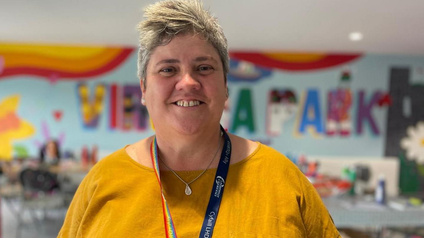 Youth homelessness coordinator Nichola Davies, in a yellow top with a work lanyard, smiles into the camera