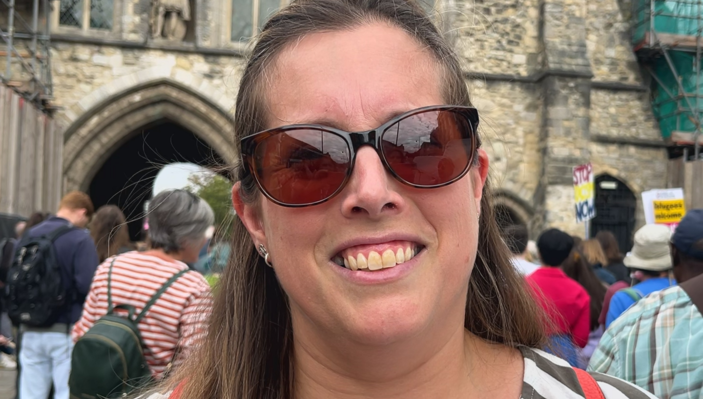 Rachel Collins has shoulder length brown hair and a black and white stripey top and is smiling for the camera. She is also wearing sunglasses 