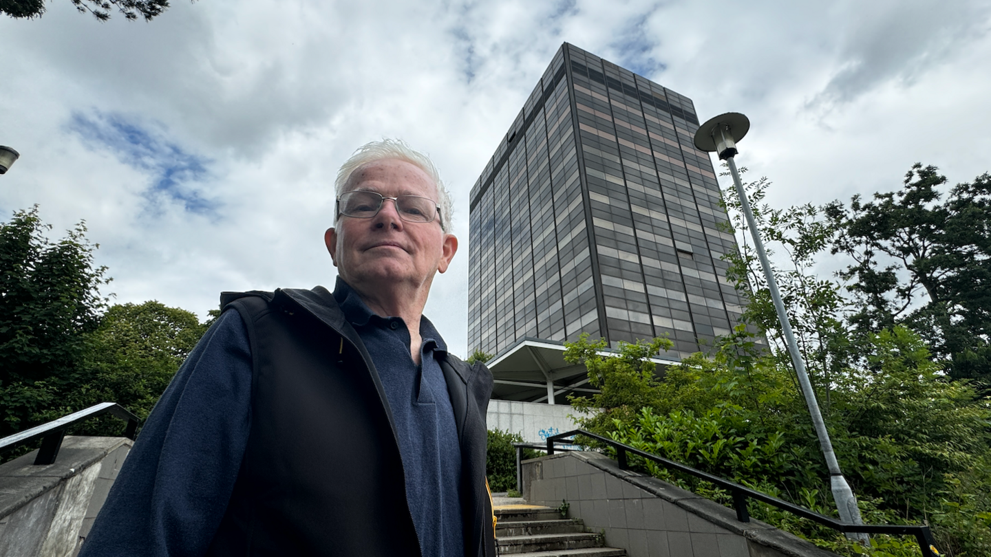 Ged Parker, who has grey hair, stands in front of tall building.