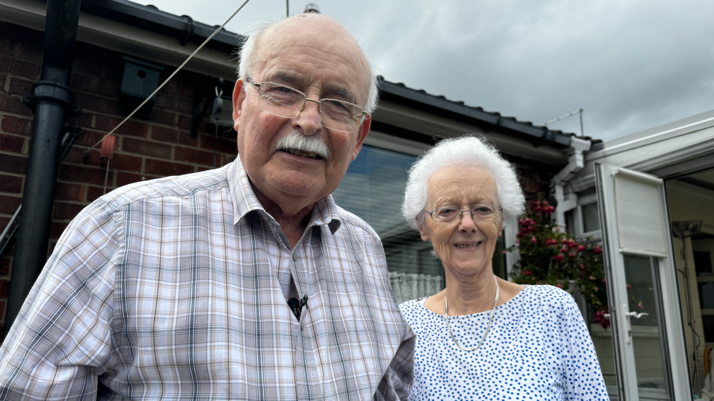 Robert and Maureen Hope, an elderly couple, outside a house.