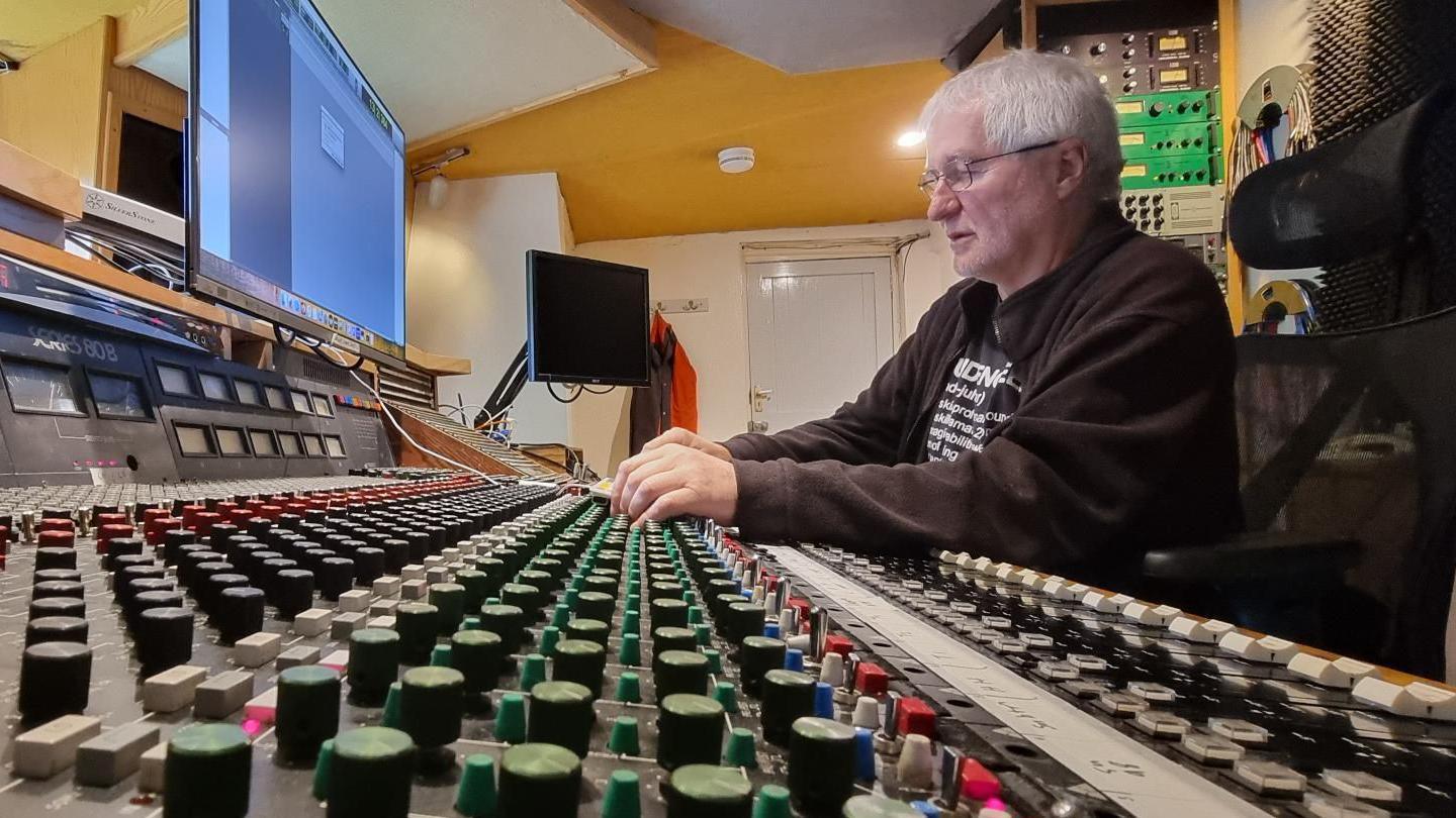 John Cornfield sat at a sound mixing desk, with screens and rows of controls around him