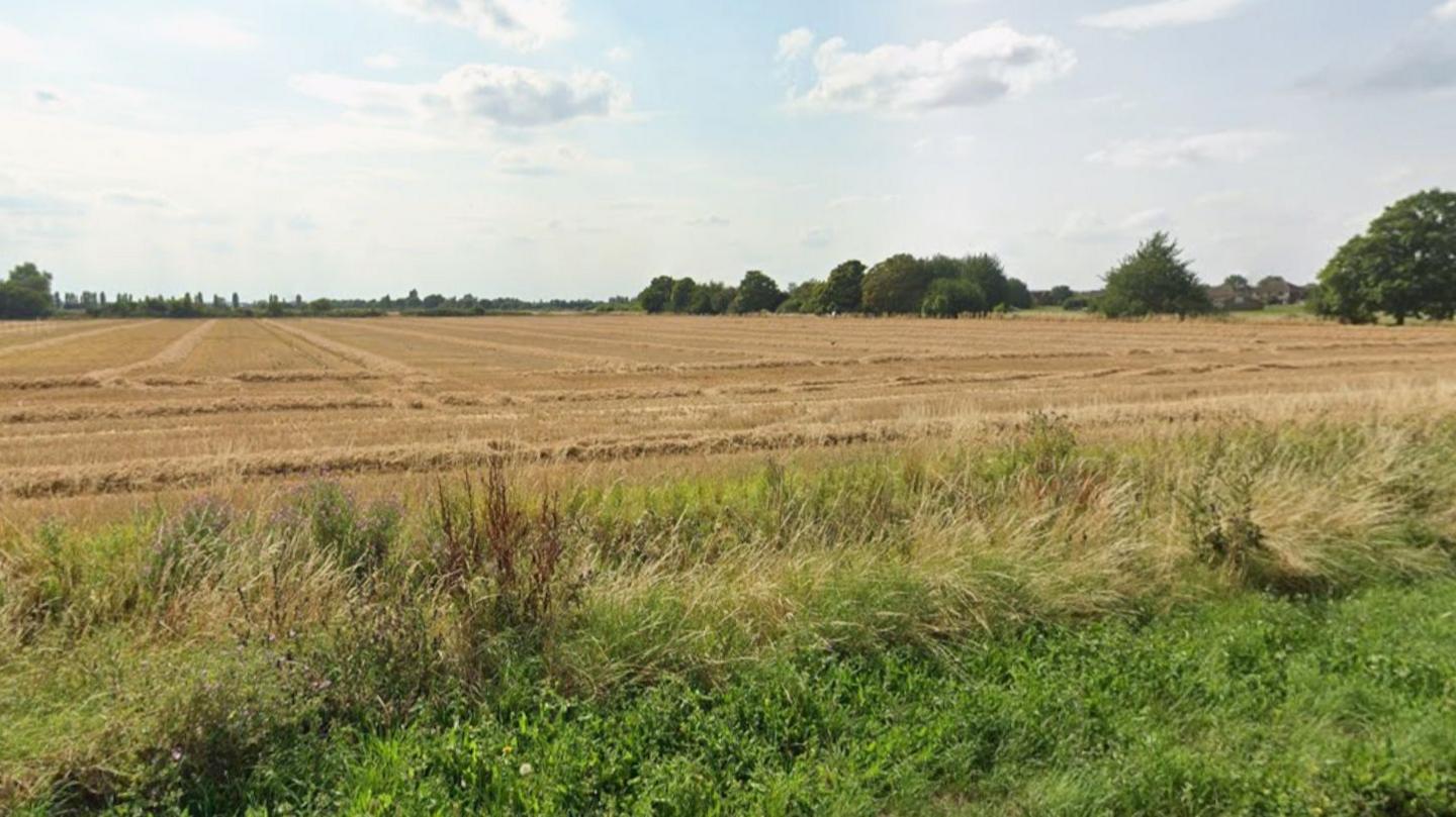 A field which has recently been harvested. There are trees around the edge of the field in the background.