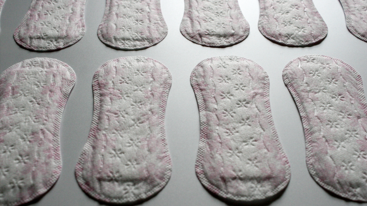 Pink and white sanitary towels laid on a white or grey surface.