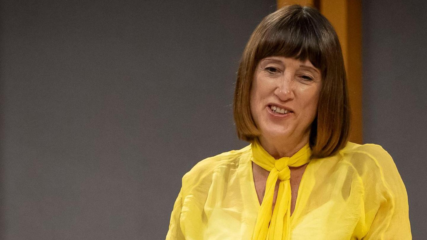 Jane Dodds wearing a yellow top smiling as she speaks in the Senedd chamber