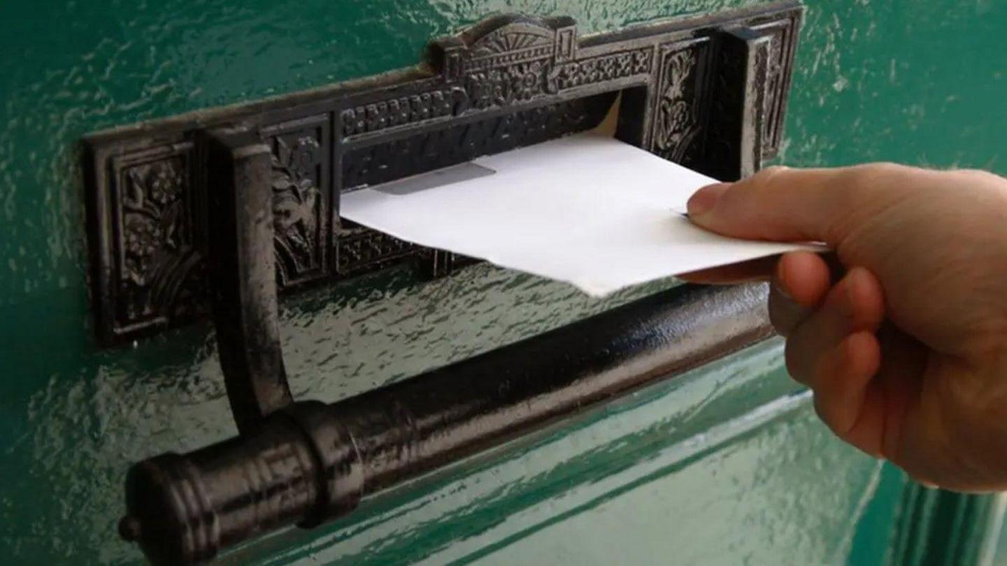 A green door with black letterbox. A letter is posted through the letterbox.