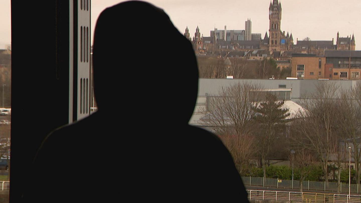 A figure in silhouette with a city scene in the background