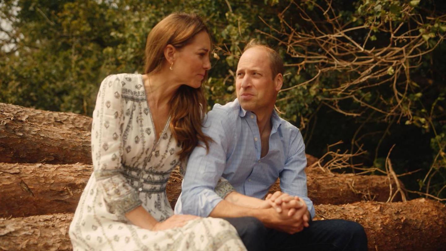 The Prince and Princess of Wales sit together holding hands. They gaze at each other adoringly