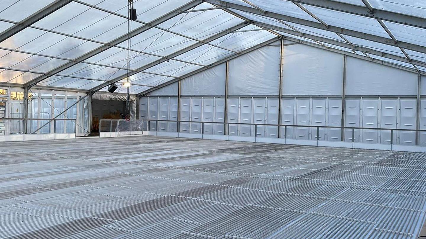 The inside of the winter ice rink which has been recently assembled. It shows a large white marquee with metal piping on the floor, before the structure has been flooded and frozen.