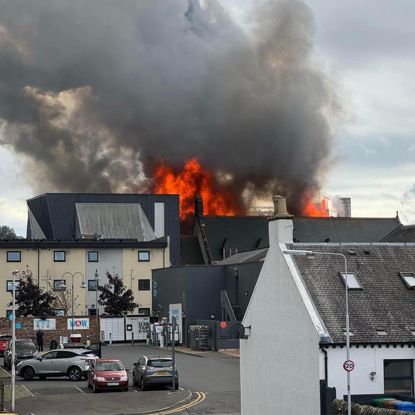 A fire at a building in Lochgelly. The fire can be seen in the building and is orange. A large plume of dark grey smoke is coming off it.