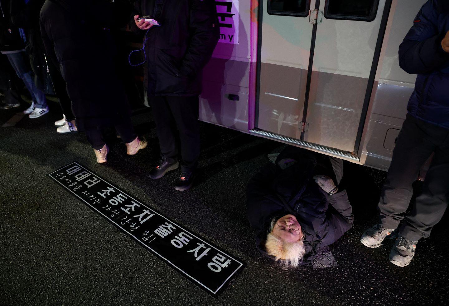 A woman lies on a road to block a vehicle transporting an army unit