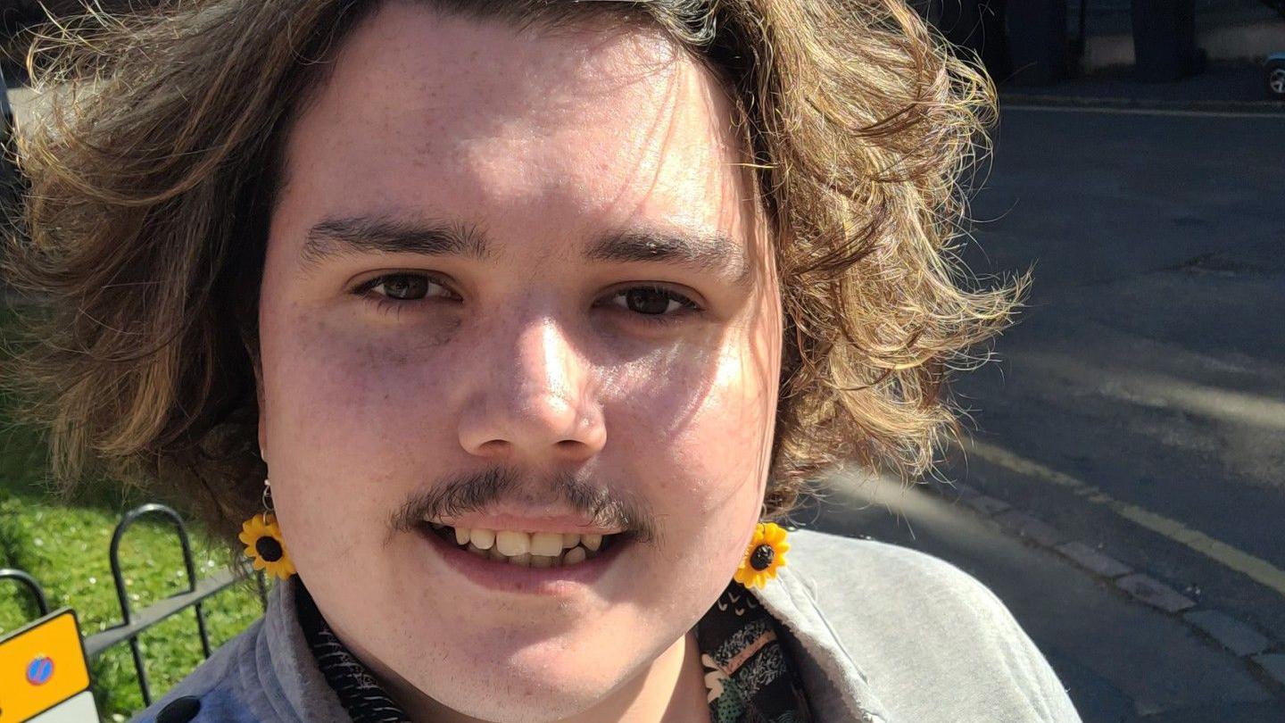 Dylan smiles in a selfie on a sunny day while wearing sunflower earrings