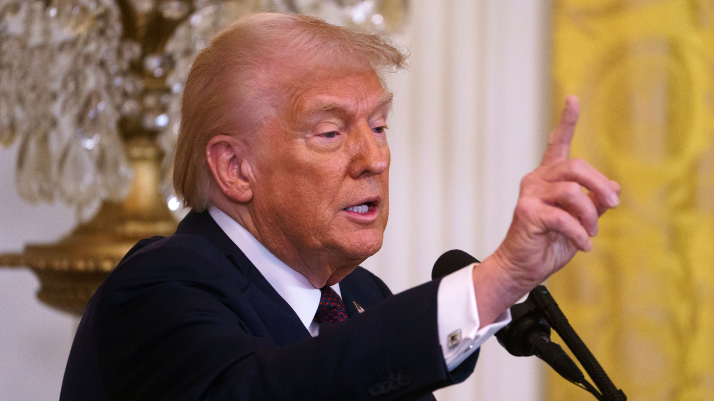 Donald Trump extending his hand at a lectern at the White House 