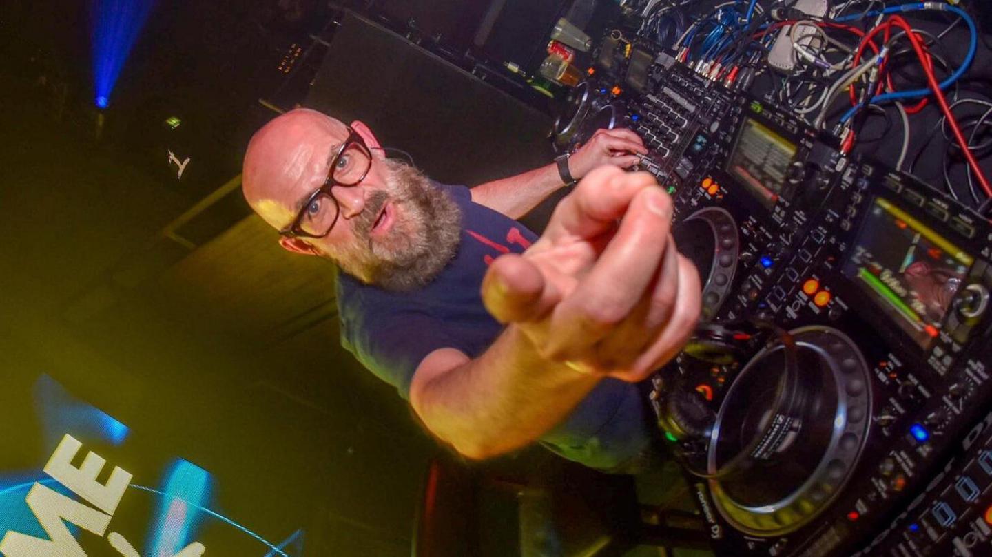 DJ Graeme Park wearing glasses and with a beard points at the camera while on the decks