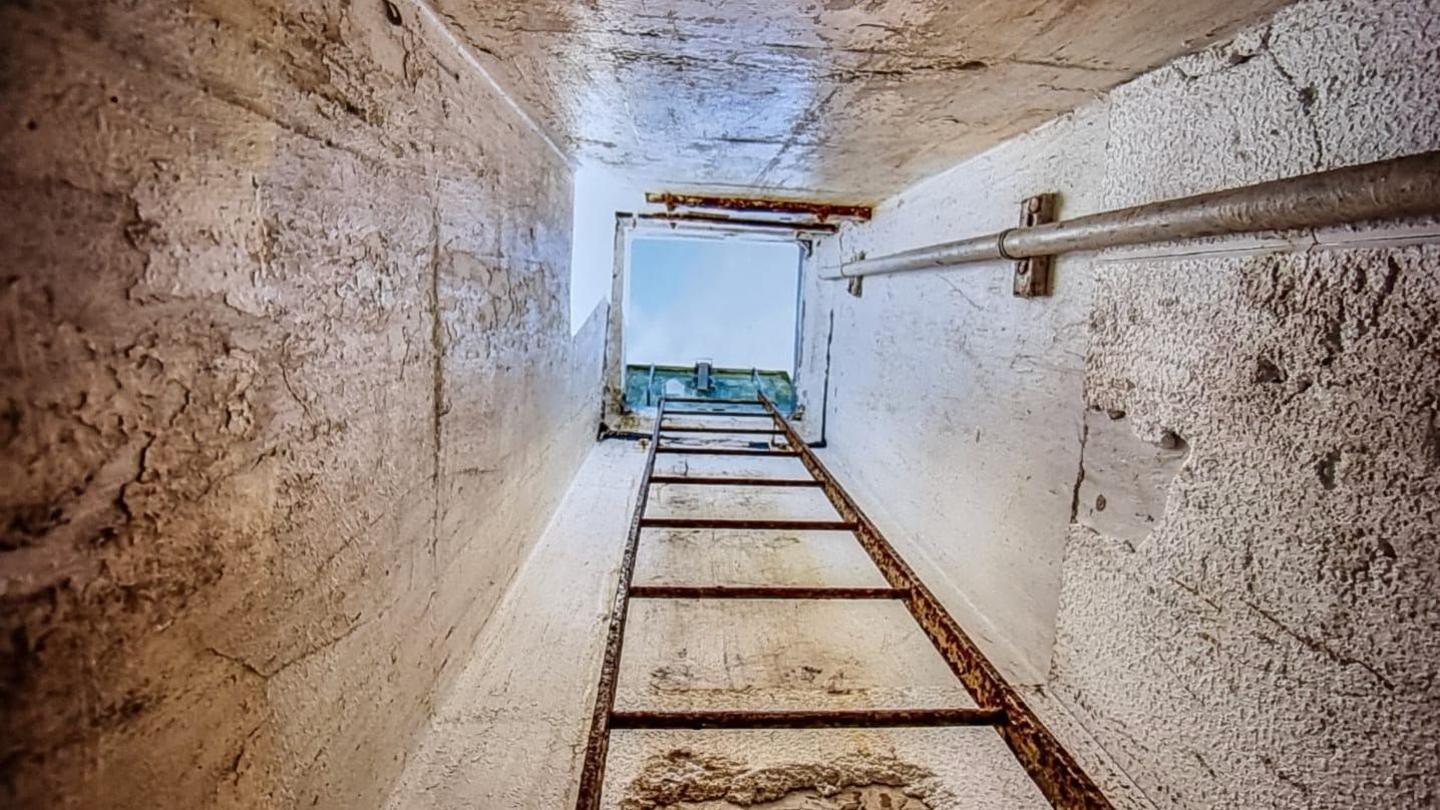 Image of a ladder down to the bunker showing a clear blue sky above