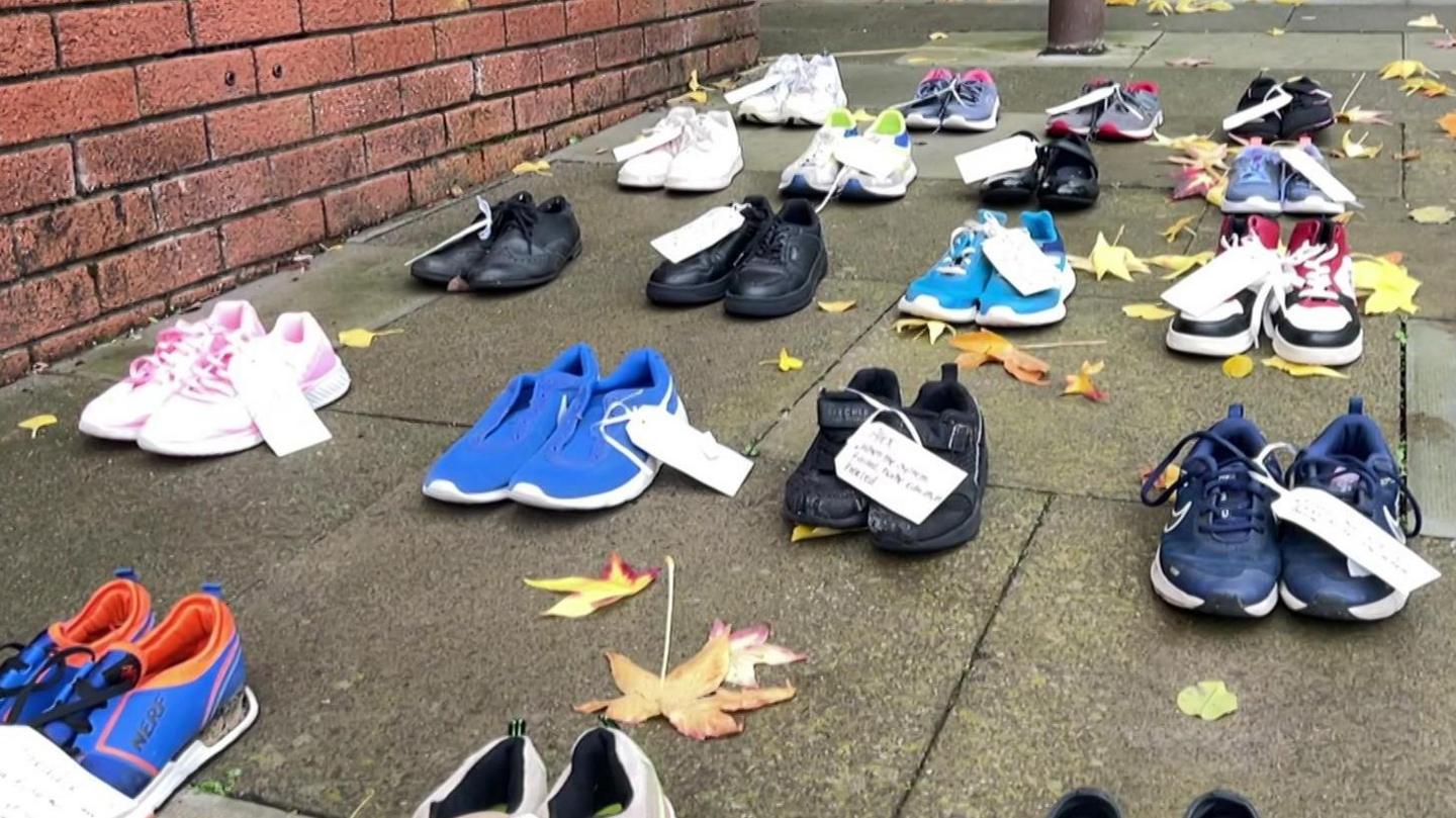 More than 15 pairs of shoes, with labels attached, laid out in lines on the pavement
