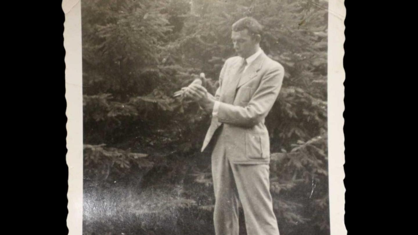 A black-and-white photo of a man dressed in a light-coloured suit holding a pigeon.