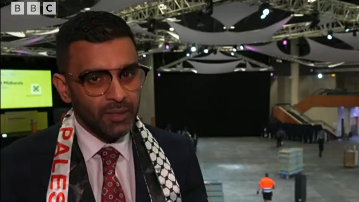 Akhmed Yakoob wearing a sash saying 'Palestine' at the vote count