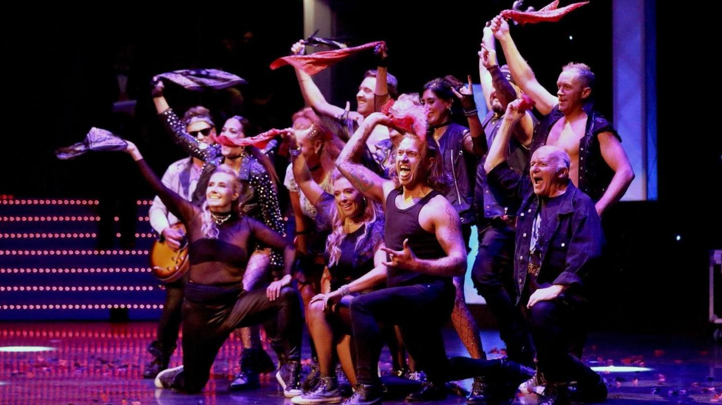 Some happy-looking dancers, men and women, whirl items of clothing around their heads.