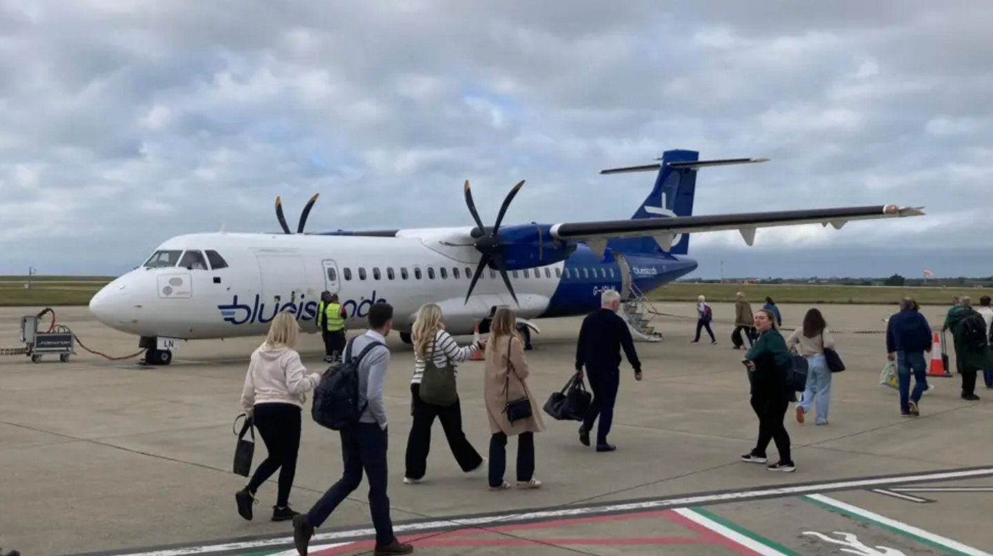 Several passengers walk along the tarmac at an airport as they board a Blue Islands plane.