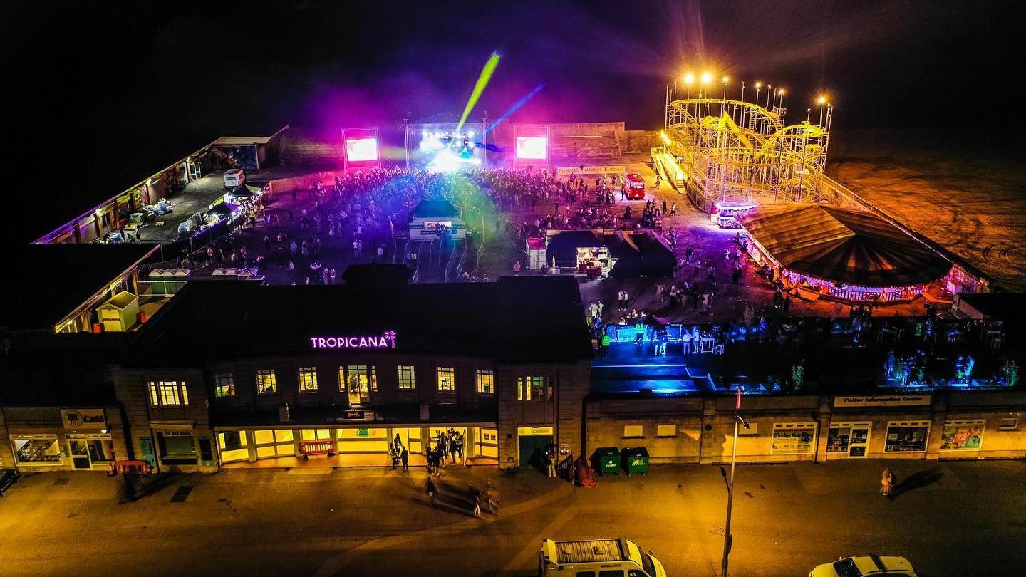 A drone shot of The Tropicana at night with a stage, lights, and a crowd watching a performance.