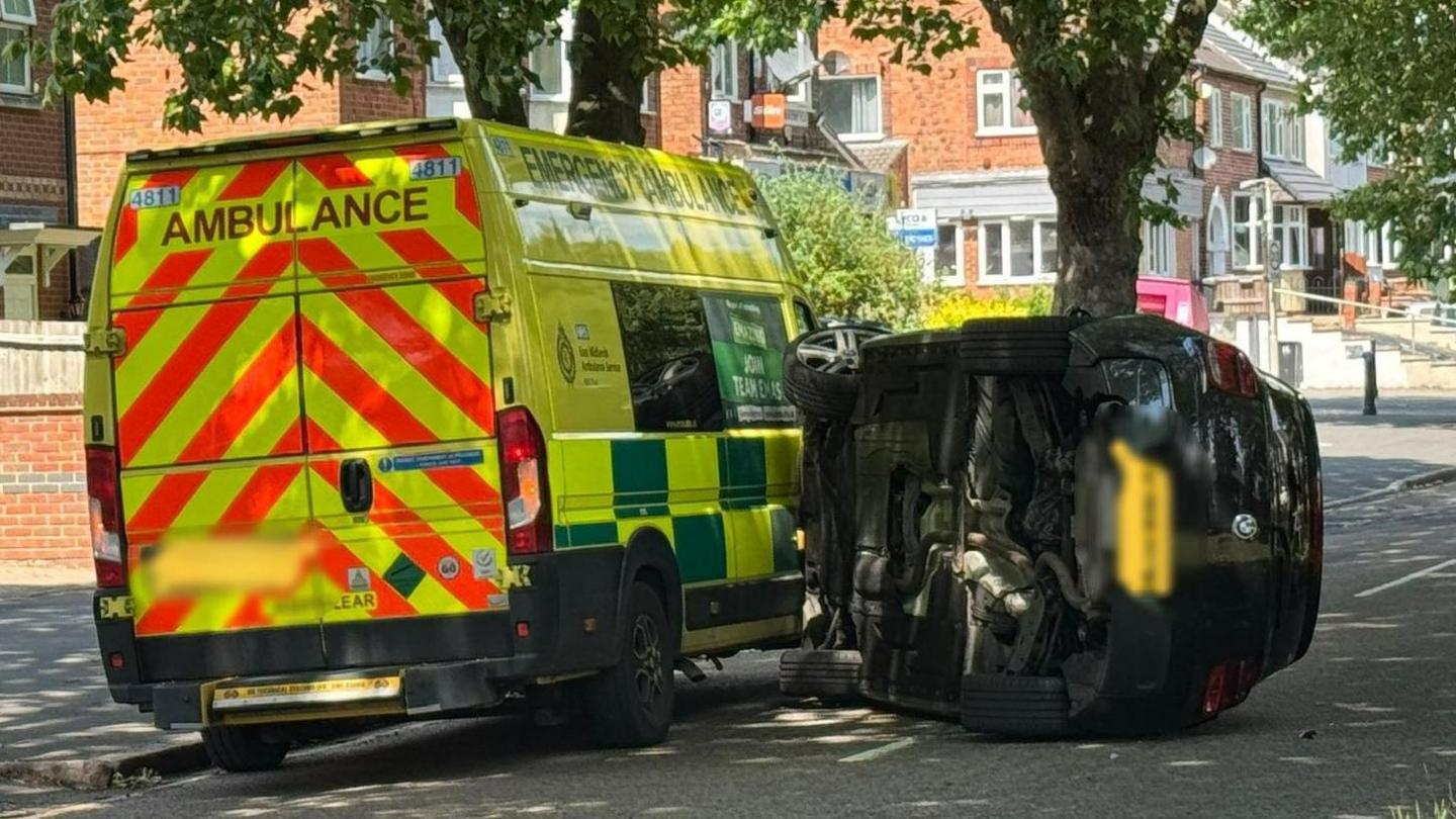 An overturned car next to an ambulance in the aftermath of a collision in Blackbird Road, Leicester.