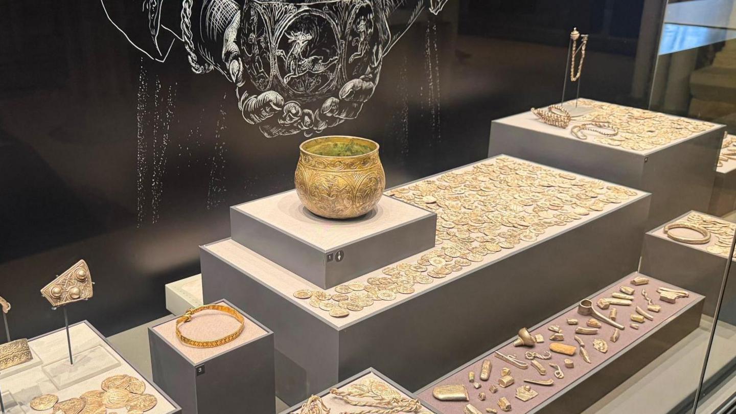 A silver bowl, coins and silver trinkets are displayed in a glass cabinet.