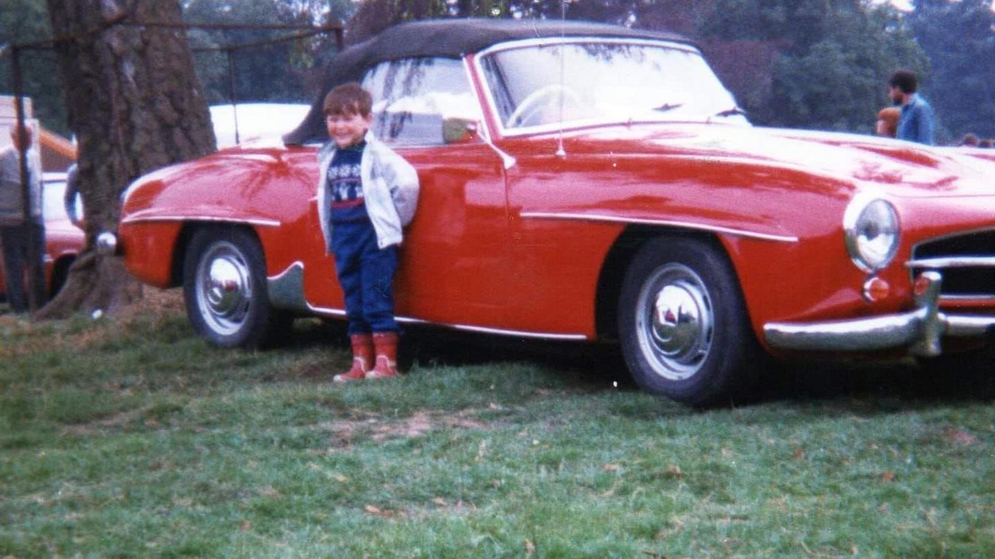 Danny Leech standing in a field beside a red vintage car.