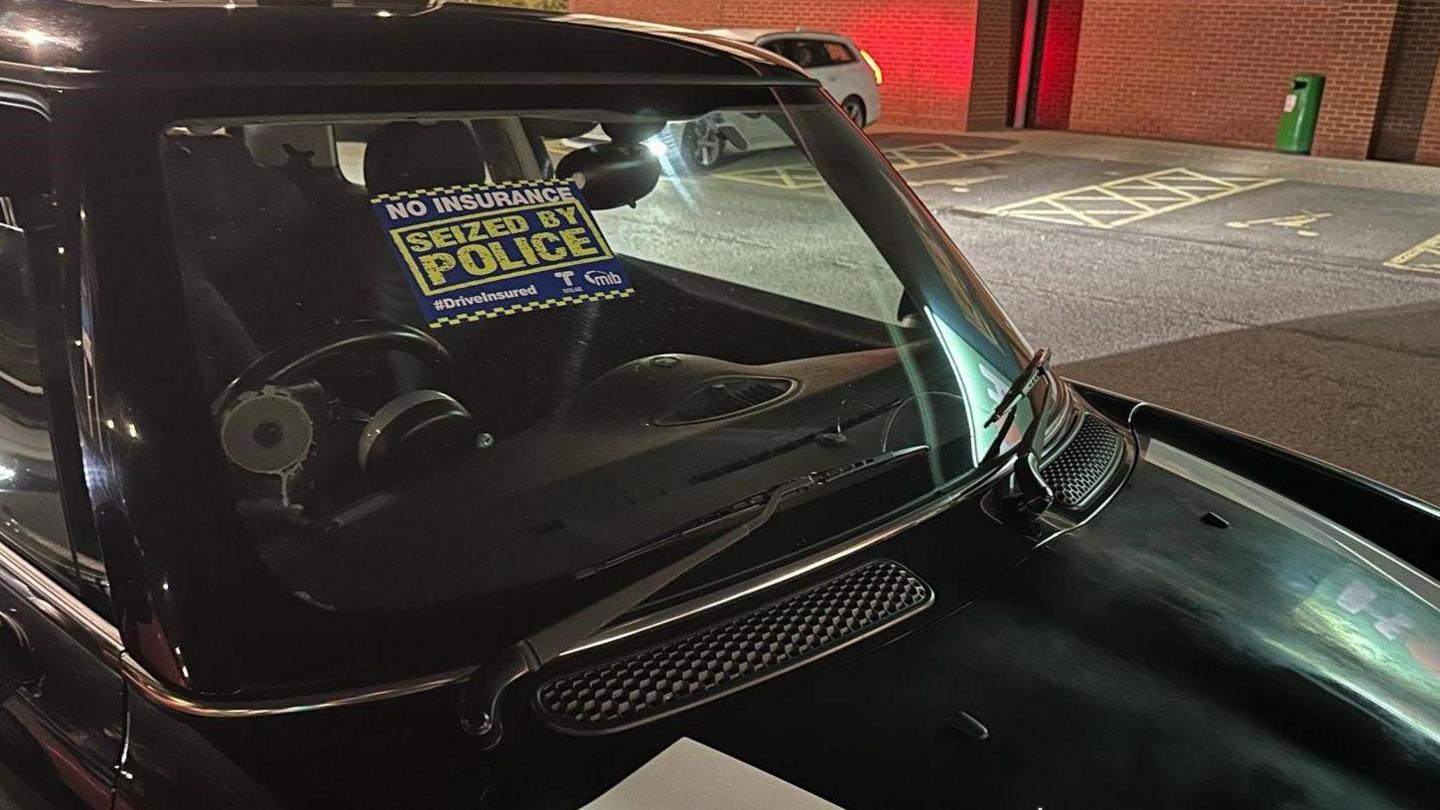 A black car with a "No insurance, seized by police" notice on the windscreen