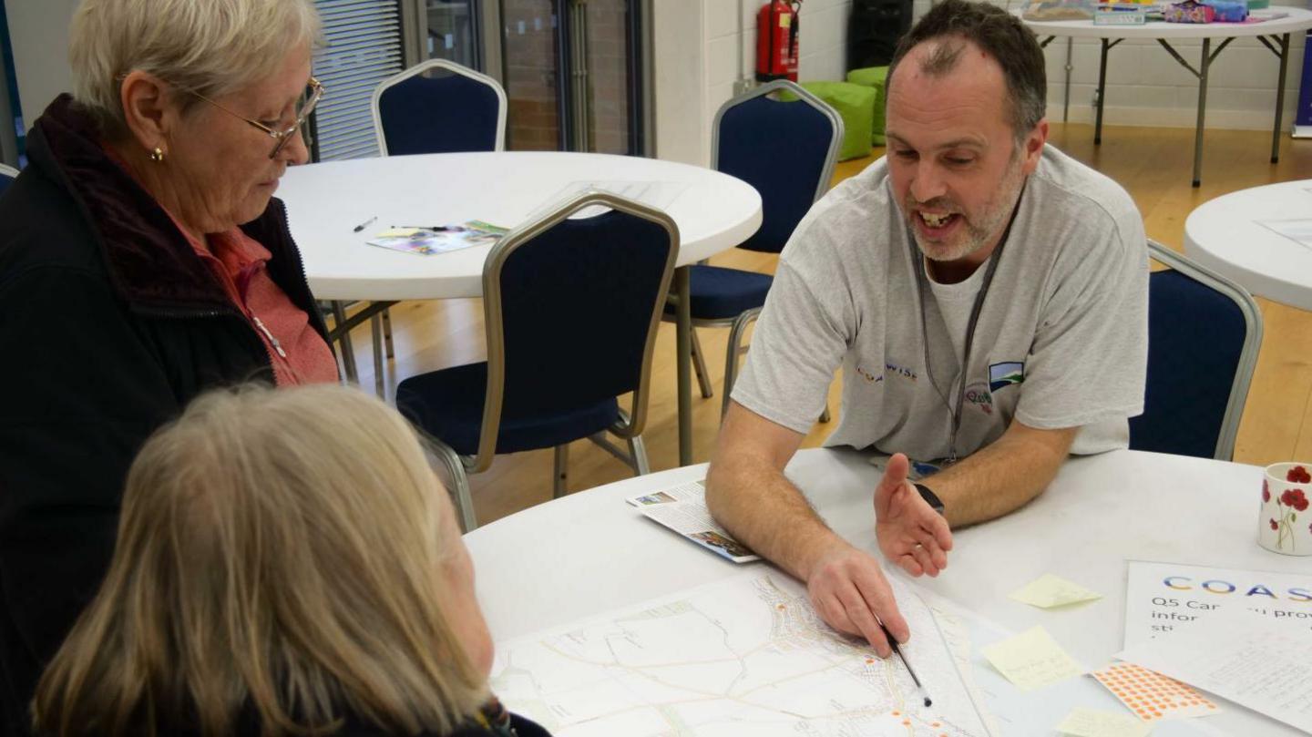 Rob Goodliffe sat at a table with two women looking at detailed plans