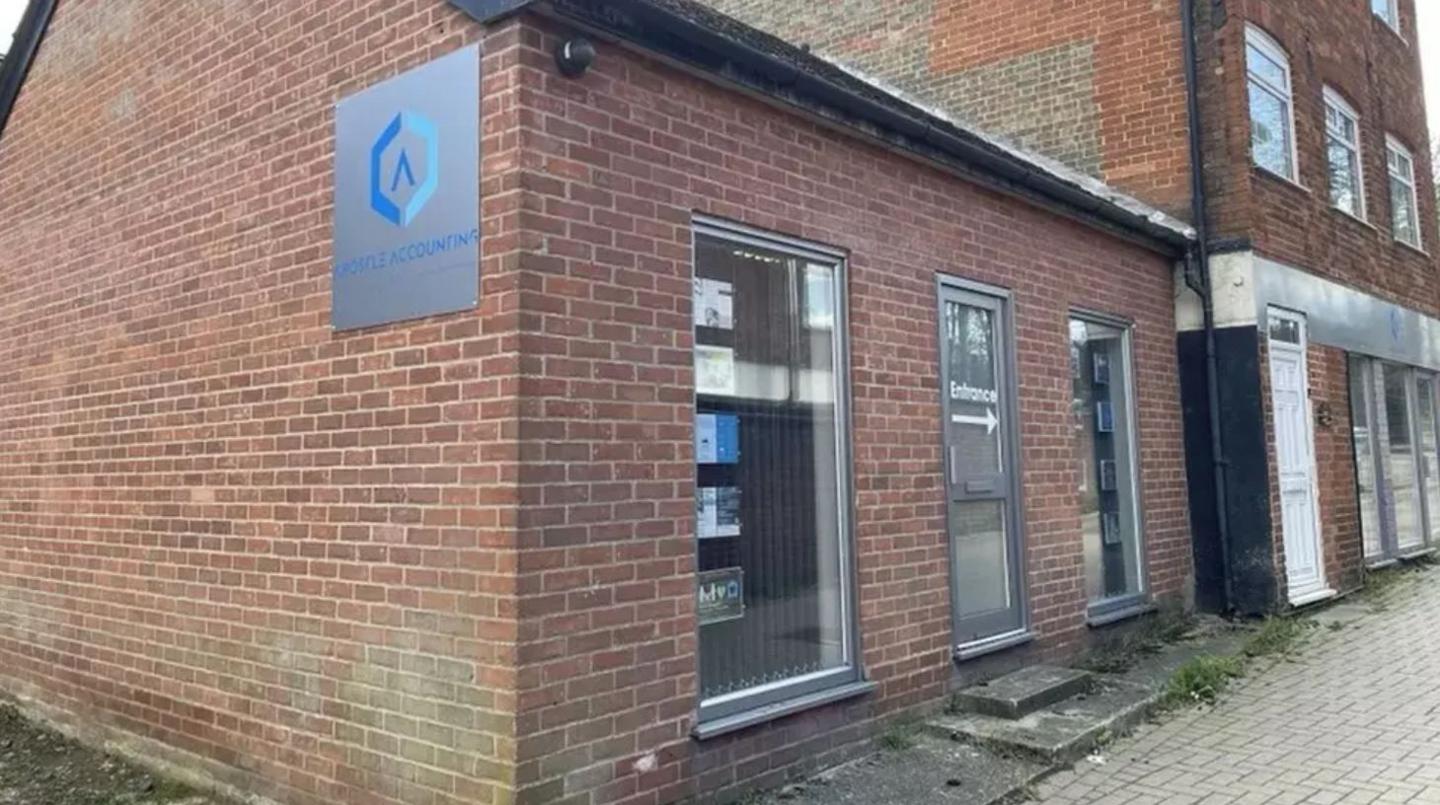 Front and side aspects of a single storey office building. The entrance and front windows are visible. The building is made out of brick and the pavement is visible out front.