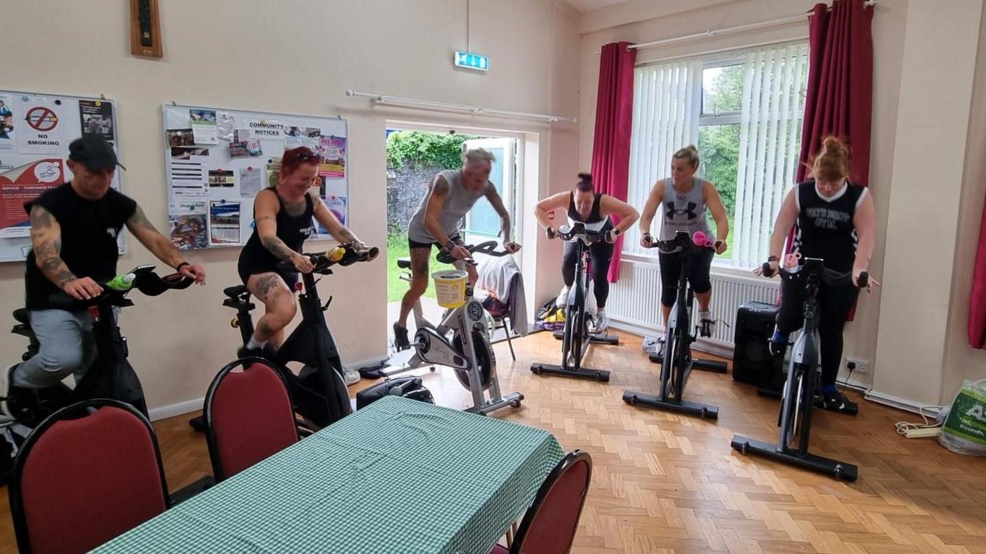 A group of people on spin bikes inside a community centre 