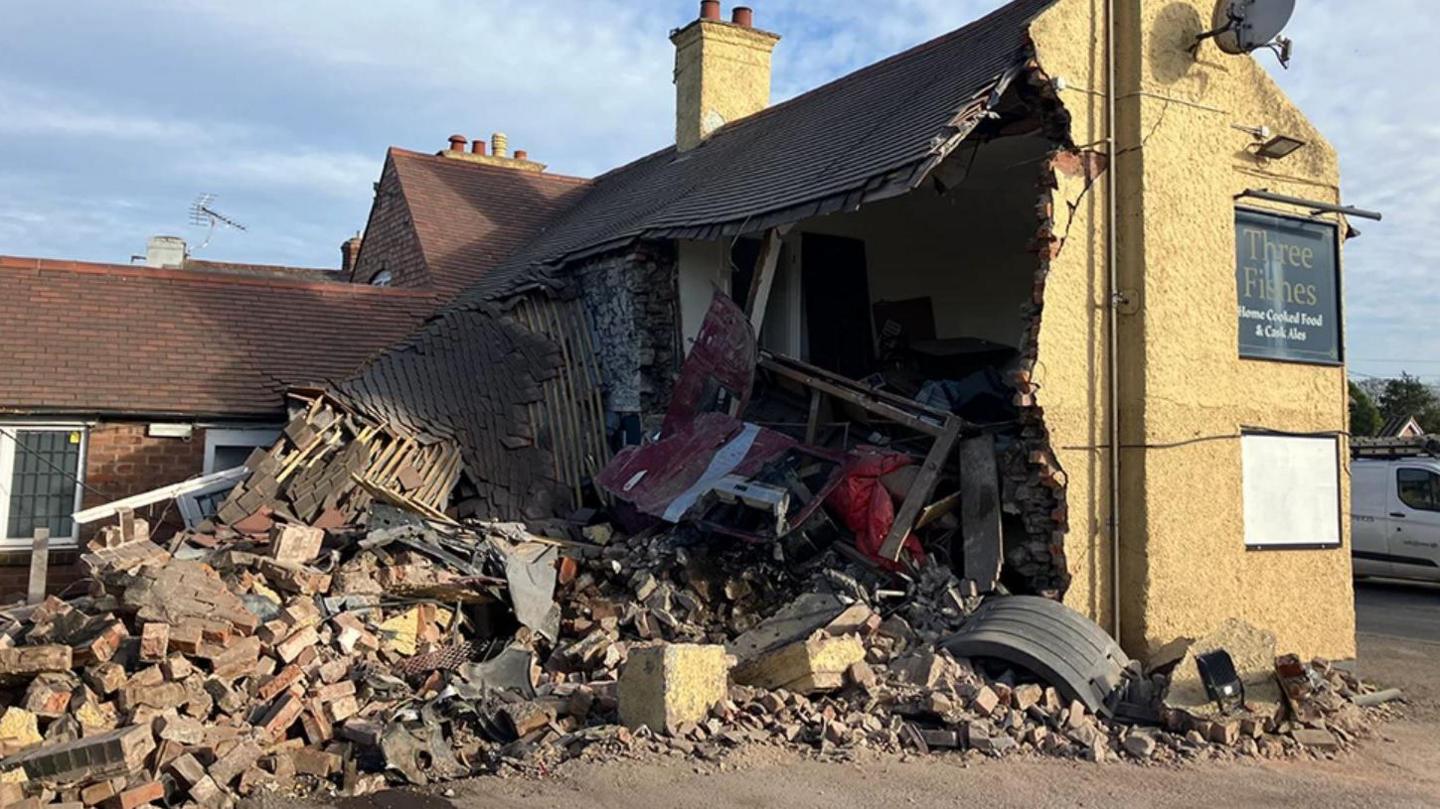 A partially demolished pub with the rear exposed and rubble covering the floor. There is a sign which reads three fishes.