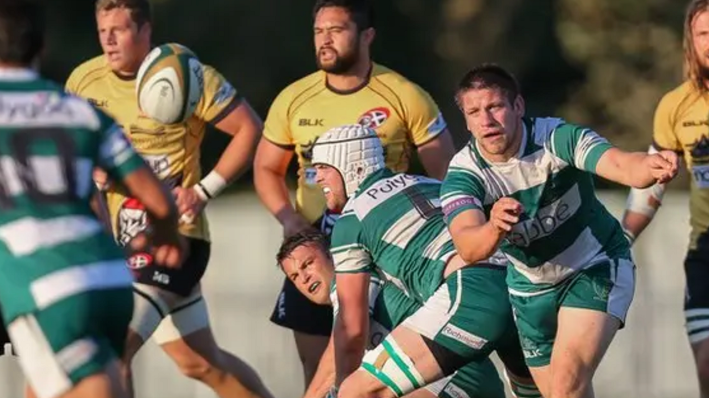 A rugby ball is thrown to a player in a white and green hooped top by another player with other players looking on.