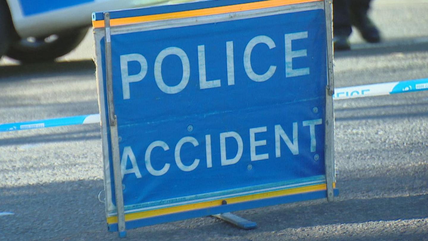 Police accident sign, white writing on blue and yellow sign, with police tape and a police vehicle behind it