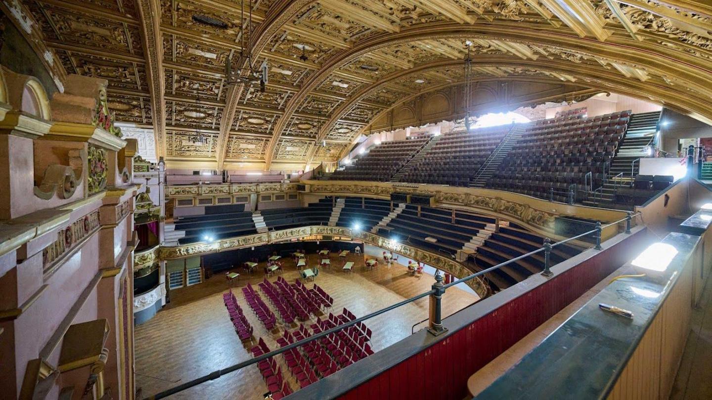 Image shows the interior of Morecambe's Winter Gardens. The stage, floor-level seating and upper tiers can be seen in the photo, taken from one of the upper tiers of the theatre.