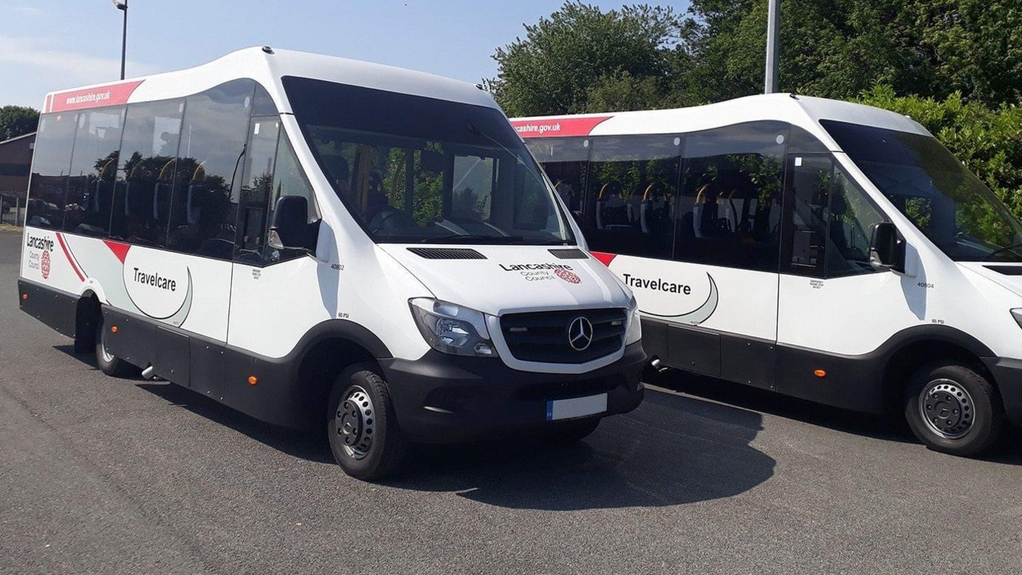 Two white minibuses side by side, with the word Travelcare printed across them.