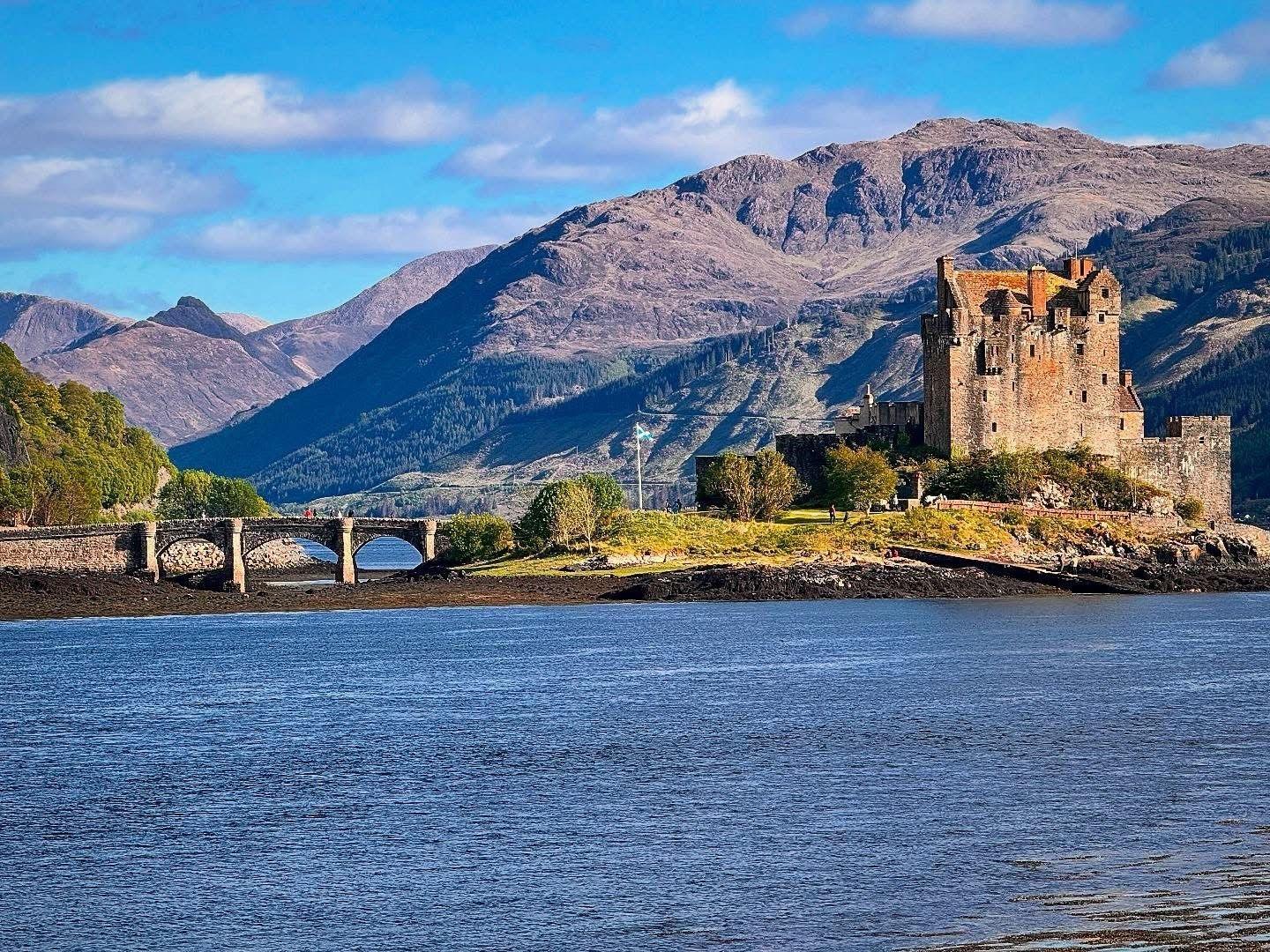 A castle with a mountain in the background and a loch in the foreground