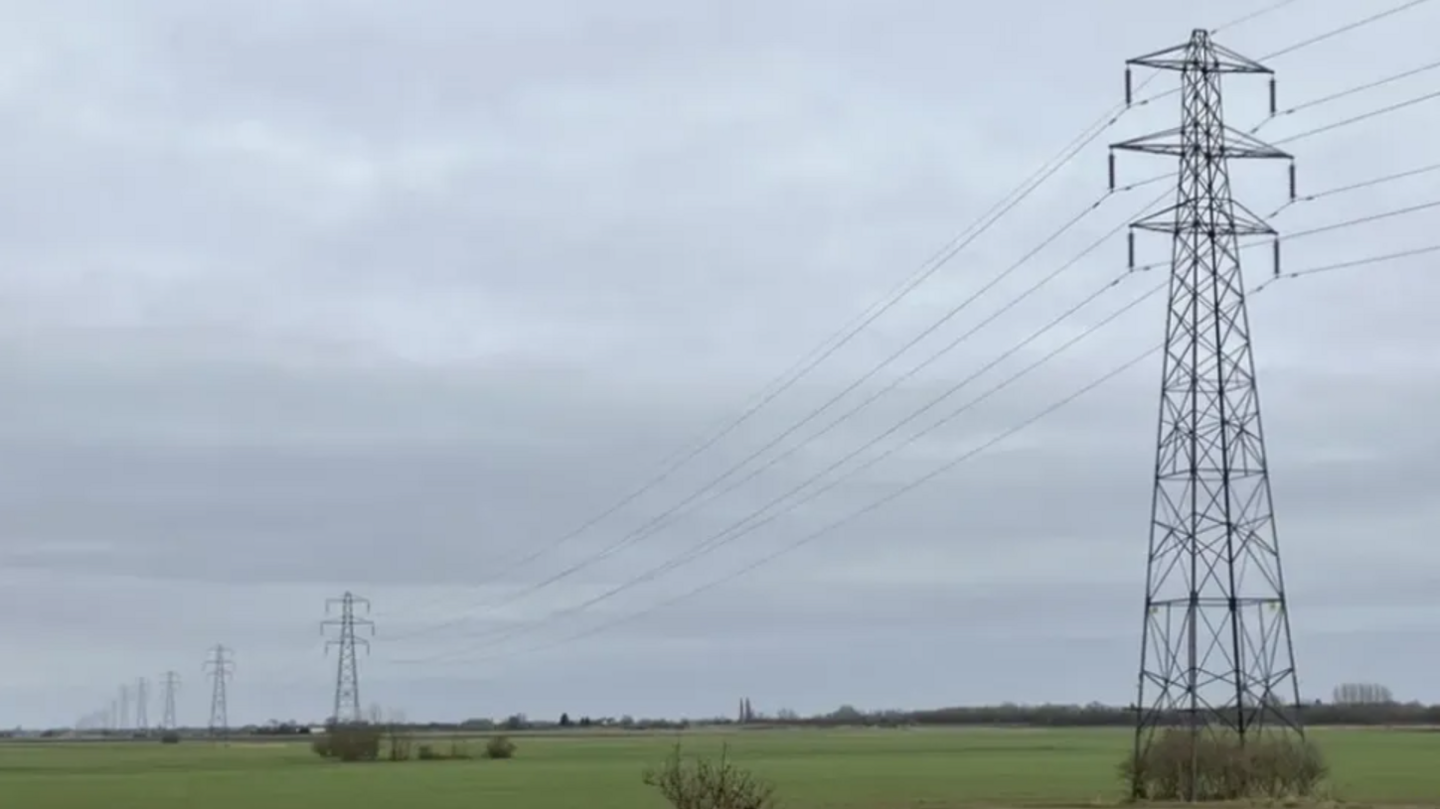 A row of electricity pylons running through countryside fields