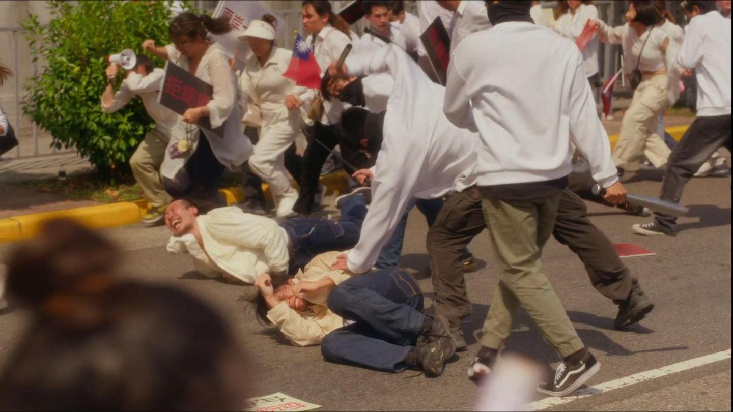 Screengrab from Zero Day Attack showing masked men in white shirts and green trousers beating up protesters on the streets of Taipei. Protesters dressed  in white tops and blue jeans are curled up on the ground screaming.