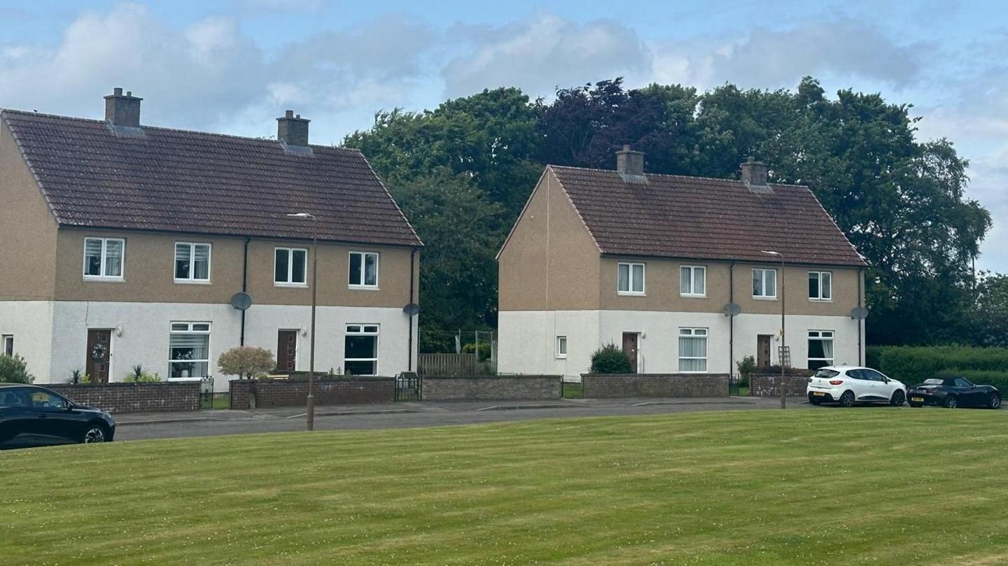 Some of the houses in Linburn Estate - a few of which are now lying empty. They are painted cream on the bottom half, brown on the first floor. Each has a brick garden wall and the grass in front is well-kept.