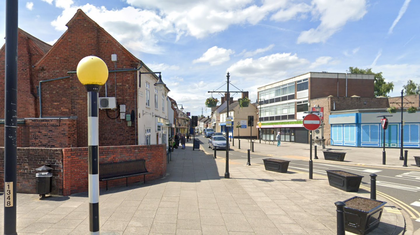 A general view of King Street in Telford. A bright day with a few clouds. There are a few buildings and the pole from a zebra crossing in view and a stop sign can also be seen. There is one car approaching a junction. 