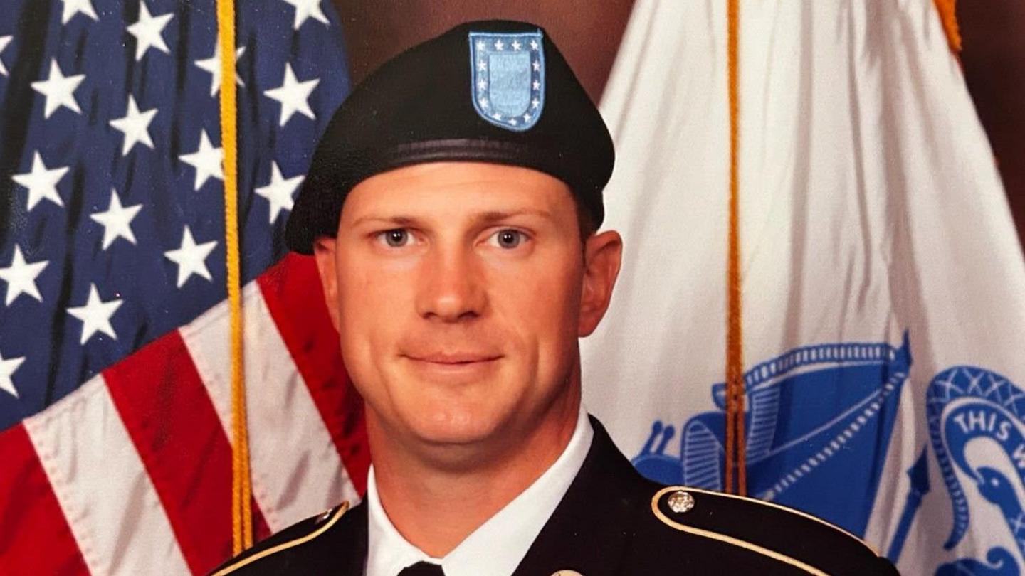 A portrait of Andrew Eaves stood in front of the American flag in his army uniform.