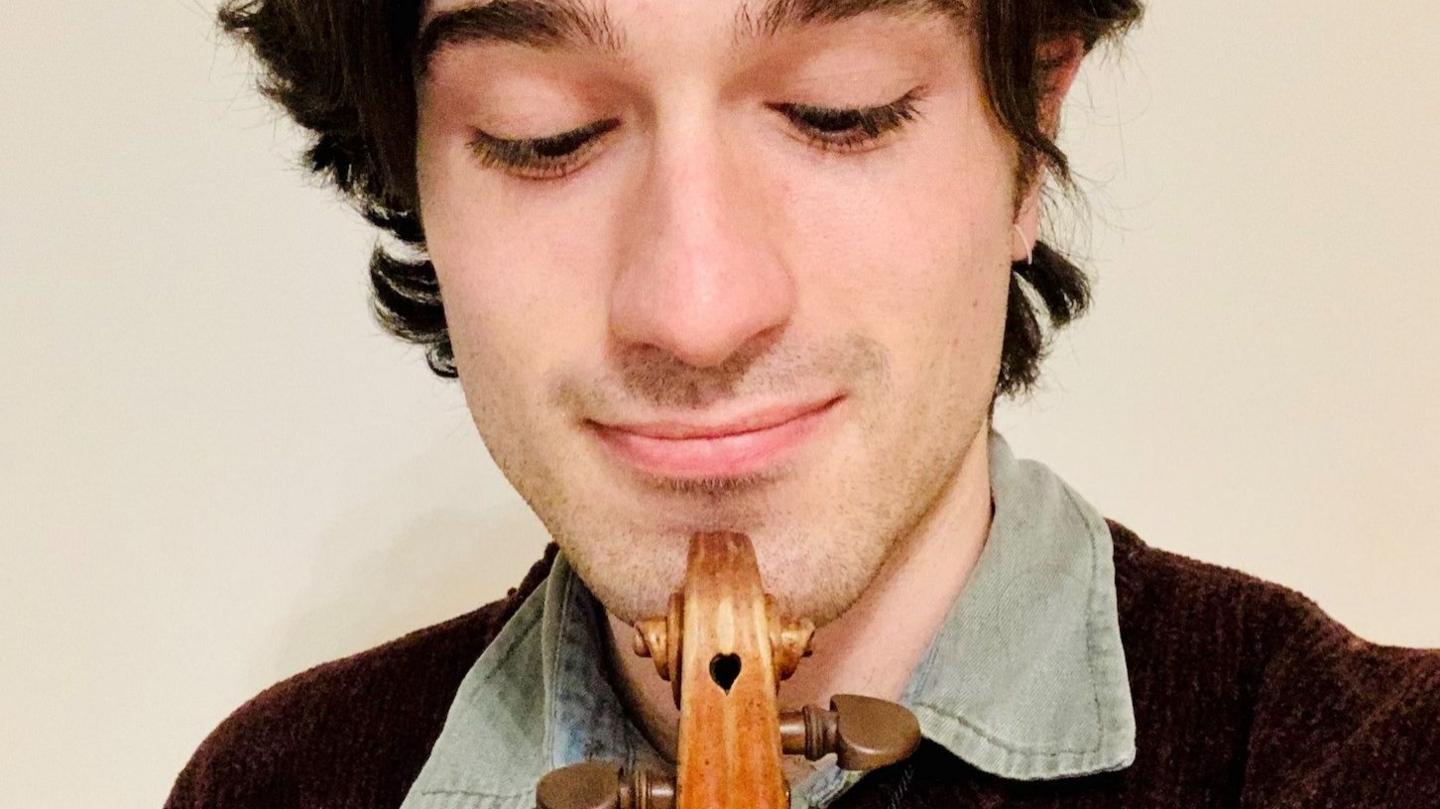 David Lopez Ibanez holds his violin to his chin as he looks down at it - the instrument has a small heart-shaped hole on top, known as the scroll, of the violin