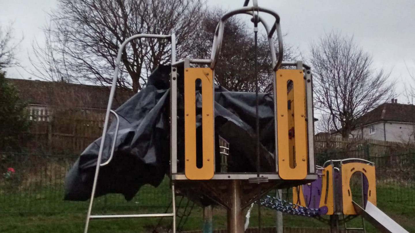 A piece of grey and yellow play park equipment is covered in a black piece of plastic.