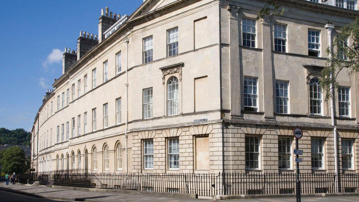 Three-storey Georgian buildings are pictured on Henrietta Street in Bath. There is a low metal fence around the buildings, which are cream coloured