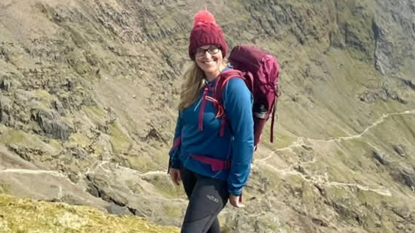 Llun o Suzie Dyer ar ochr mynydd, wedi gwisgo yn addas i gerdded y mynyddoedd