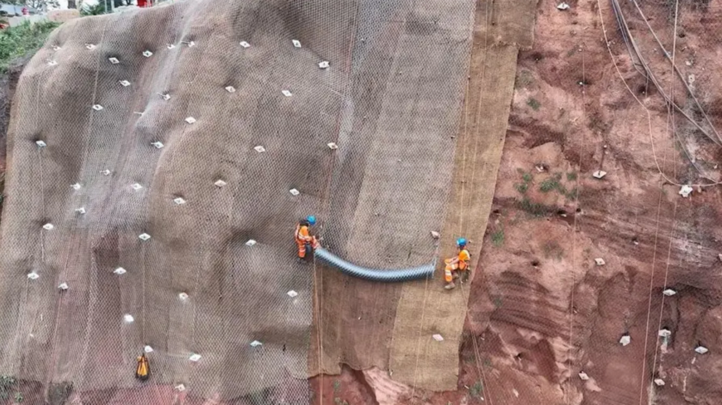 Two men are seen suspended on a cliff face on top of a protective netting during works for the Dawlish to Holcombe Cliff Stabilisation