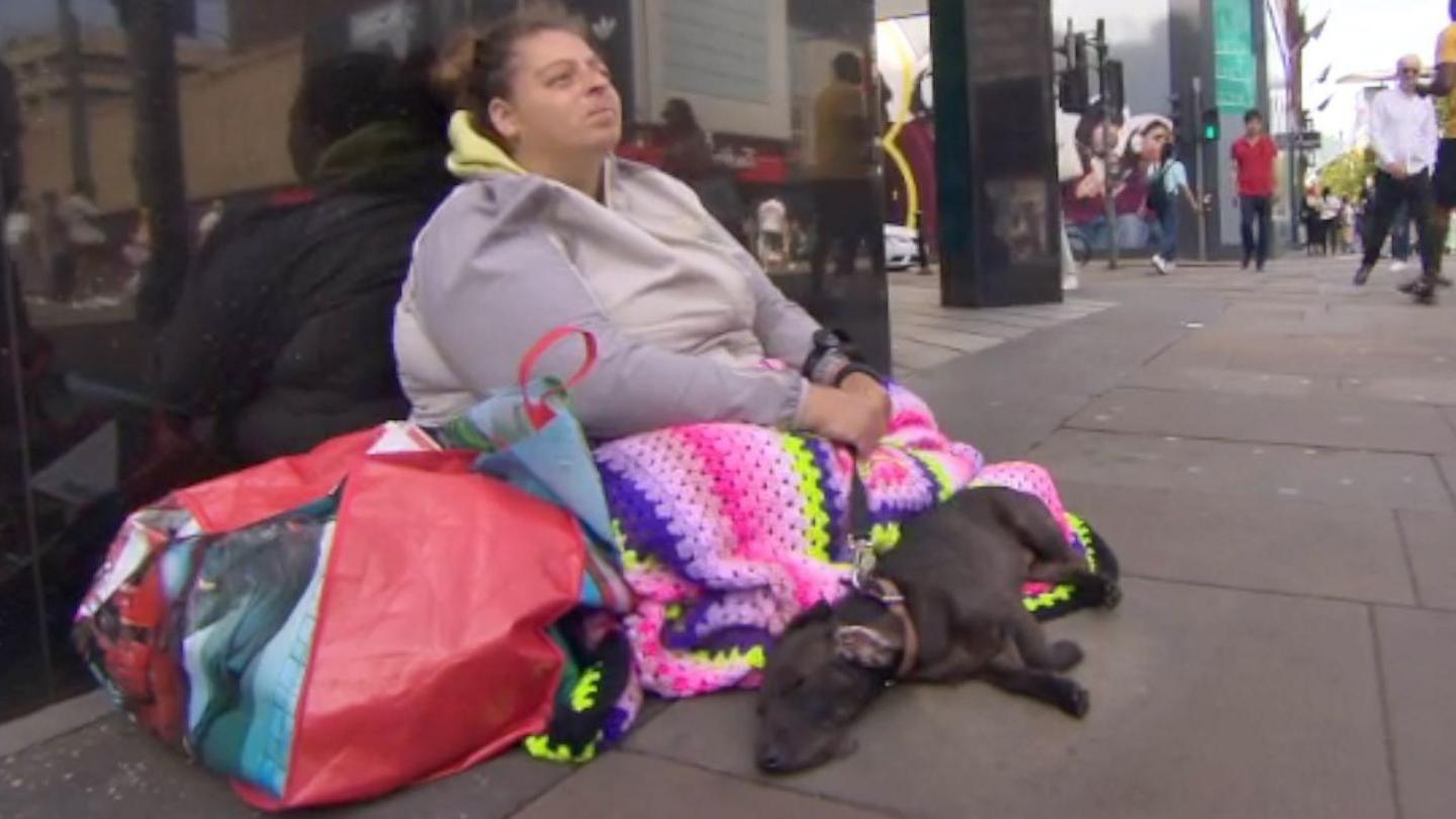 Adele, a homeless woman living in Manchester, sits outside a high street  department store, her knees covered by a colourful blanket and her Labrador Belle lying at her feet